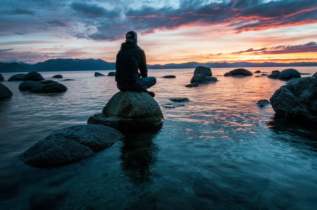 man sitting on a rock meditating while facing the sky